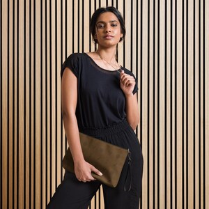 May include: A woman wearing a black short-sleeved shirt and black pants is holding a brown clutch purse with a black strap.