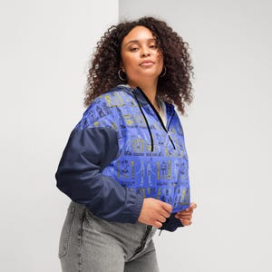May include: A blue and black cropped jacket with a zipper closure and a pattern of Egyptian hieroglyphs in gold. The jacket has a hood.
