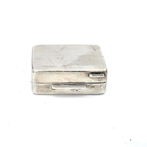 May include: A small, rectangular silver box with a textured lid and a hinged closure. The box is likely vintage, with a slightly tarnished appearance. The design is simple and elegant, suitable for storing small items.