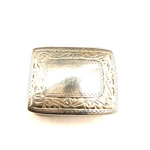 Puede incluir: Hebilla de cinturón rectangular plateada con un diseño floral ornamentado. La hebilla tiene un área rectangular central y está rodeada de intrincados adornos. El metal tiene un aspecto ligeramente deslustrado.