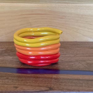 May include: A stack of colorful, coiled ceramic rings in shades of red, orange, and yellow. The rings are stacked on a wooden surface.