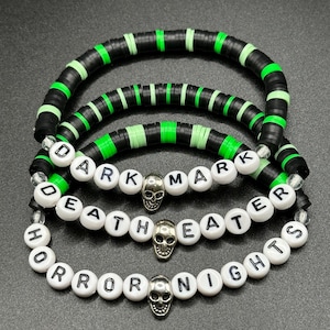 May include: Three bracelets with a dark theme. The top two bracelets are black and green disc beads. The bottom bracelet has white letter beads spelling "DEATH MARK" and "HORROR NIGHTS" with skull charms.