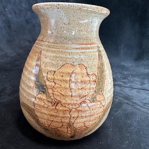 May include: A ceramic vase with a speckled brown glaze and a hand-painted design of a flower with green leaves.