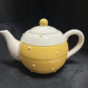 May include: A yellow and white ceramic teapot with a round body and white polka dots. The teapot has a lid with a yellow knob.