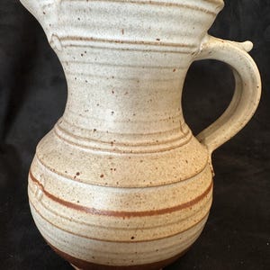 以下が含まれることがあります： 茶色の縞模様と斑点のある白い陶器のピッチャー。ピッチャーは口が広く、取っ手があります。