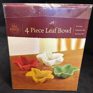 May include: A box set of four leaf-shaped bowls in red, white, yellow, and green. The box reads "4 Piece Leaf Bowl" and "Dishwasher Safe Microwave Safe". The bowls are arranged on a wooden surface.