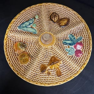 Peut inclure: Un plat de service rond en céramique avec un motif de panier tissé. Le plat comporte cinq sections, chacune décorée d'un aliment différent : des pois, une noix, un champignon, une baie et un coing. Le plat est brun avec des accents verts, rouges et blancs.