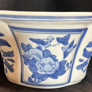 May include: White ceramic planter with blue floral and bird designs. The planter has a wide, octagonal shape with a blue band around the rim. The blue design includes flowers, leaves, and birds.