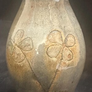 May include: A handmade ceramic vase with a flared rim and a textured, mottled finish in shades of gray and brown. Two stylized flower designs are etched into the vase. The vase is approximately 8 inches tall.