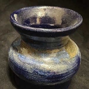 Op de afbeelding: Een handgemaakte keramische vaas met een donkerblauwe glazuur. De vaas heeft een brede, open bovenkant en een bolvormig lichaam, met een textuur. De kleur gaat over van donkerblauw naar lichtere tinten, met gouden accenten.