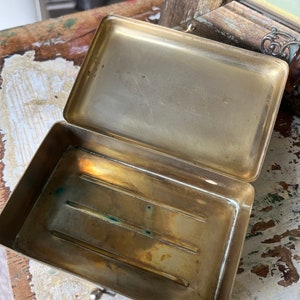 Puede incluir: Una caja de lat&oacute;n con tapa abatible y un peque&ntilde;o pestillo. El interior de la caja tiene tres ranuras. La caja est&aacute; vac&iacute;a.
