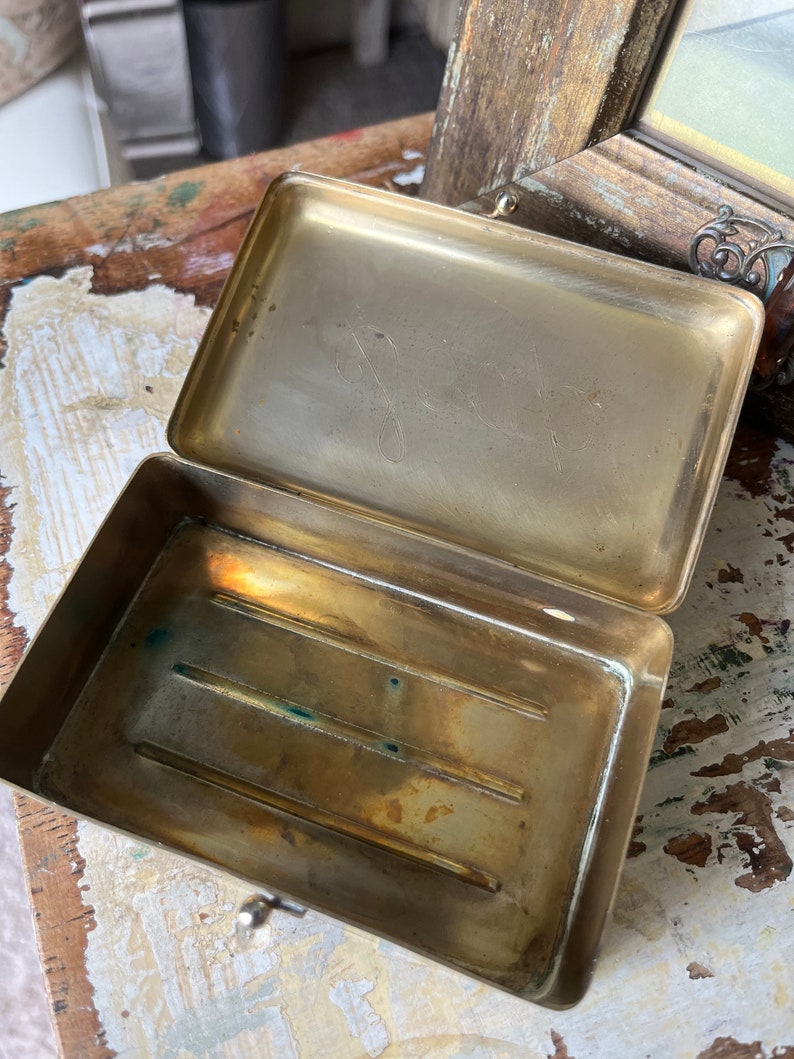 Puede incluir: Una caja de lat&oacute;n con tapa abatible y un peque&ntilde;o pestillo. El interior de la caja tiene tres ranuras. La caja est&aacute; vac&iacute;a.