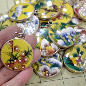 May include: A collection of round, yellow enamel pendants with floral and butterfly designs. The pendants have silver rims and are strung on a silver chain.