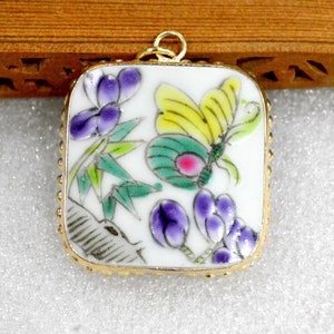 May include: A square porcelain pendant with a gold-tone frame. The pendant features a hand-painted design of a butterfly with yellow and green wings, purple flowers, and green bamboo stalks.