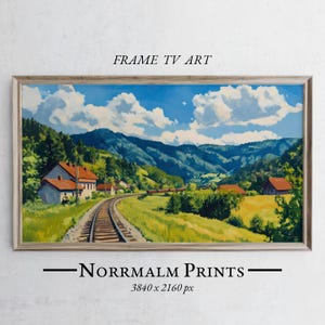 Op de afbeelding: Een schilderij van een spoorlijn die door een groene vallei slingert met huizen en bergen op de achtergrond. De lucht is blauw met witte wolken. Het schilderij is ingelijst in een licht houten lijst.
