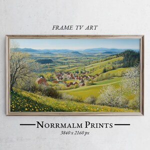 May include: A framed landscape print depicting a village in a valley, with green hills and mountains in the background. The artwork is in a natural wood frame and includes the text "FRAME TV ART" and "-Norrmalm Prints-"