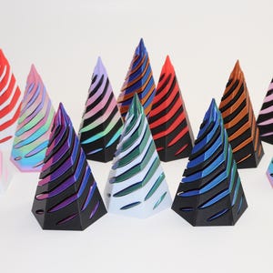 May include: A collection of ten colorful, geometric, pyramid-shaped ornaments with a layered, striped design. The ornaments are made of a shiny, iridescent material and are arranged in a row on a white surface.
