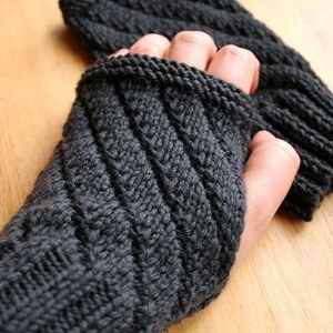 May include: Dark gray knitted fingerless gloves with a textured, diagonal ribbed pattern. The gloves are made of a soft, warm material, perfect for cold weather. The design features a comfortable fit, ideal for everyday wear.