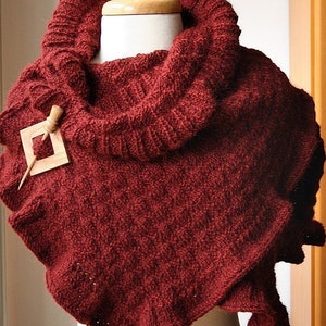 May include: A maroon knitted cowl scarf with a wooden pin and a decorative wooden piece. The scarf is draped over a white mannequin.