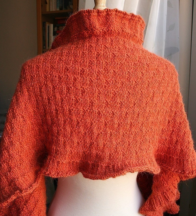 May include: A burnt orange knitted shawl with a high neck and ruffled edges.