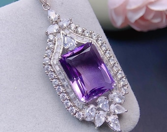 May include: A silver pendant with a large, rectangular, purple amethyst gemstone surrounded by smaller, clear, round gemstones. The pendant has a detailed, ornate design.