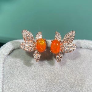 Può includere: Un paio di orecchini a forma di farfalla con pietre preziose di opale arancione e dettagli in zircone cubico trasparente. Gli orecchini sono realizzati in metallo placcato oro rosa.