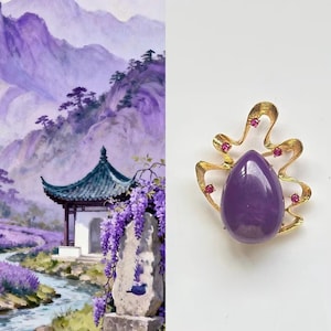 May include: A gold brooch with a large, teardrop-shaped purple gemstone. The brooch has a decorative, organic design with small, round red gemstones. The background shows a landscape painting of a purple mountain scene with an Asian-style building.