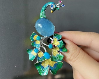 Peut inclure: Une broche en argent en forme de paon avec une pierre d'aigue-marine bleue et des accents turquoise. Les plumes de la queue du paon sont vertes, jaunes et dorées.
