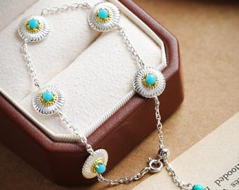 Può includere: Bracciale in argento con dettagli turchesi e dorati. Il bracciale presenta un design a catena con cinque ciondoli circolari a forma di fiore. Ogni ciondolo ha un centro turchese circondato da dettagli in oro e argento. Il bracciale è presentato in un cofanetto marrone.