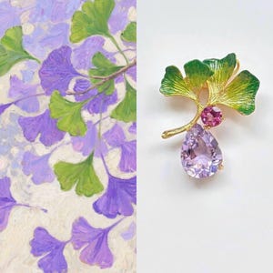 Könnte beinhalten: Goldfarbene Brosche in Form eines Ginkgoblattes mit grünen Emaille-Details. Die Brosche hat einen kleinen rosa Edelstein und einen großen, birnenförmigen, hellvioletten Edelstein. Der Hintergrund ist ein Gemälde aus lila und grünen Blättern.