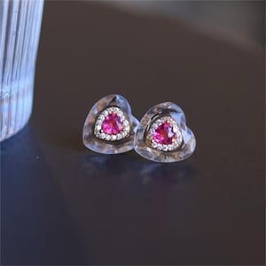 May include: A pair of heart-shaped earrings with a clear crystal setting and a pink gemstone in the center.