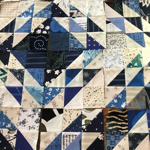 May include: A quilt made of blue and white fabric squares and triangles. The fabric has various patterns, including floral, geometric, and text.