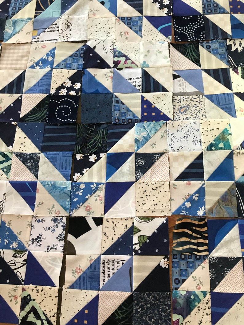 May include: A quilt made of blue and white fabric squares and triangles. The fabric has various patterns, including floral, geometric, and text.