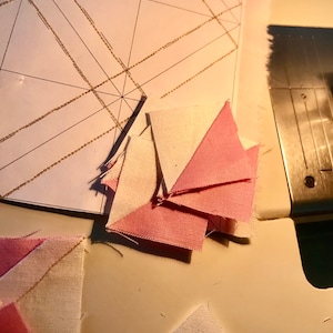 May include: A close-up of pink and white fabric squares, cut and ready to be sewn together. The fabric squares are arranged in a pile on a white surface.