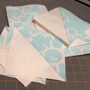 Puede incluir: Una colección de cuadrados de tela blanca y azul claro, algunos con un patrón floral, dispuestos en un patrón en capas sobre una estera de corte.