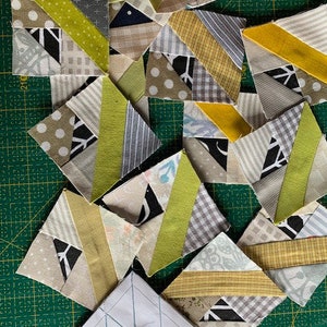 May include: A collection of fabric squares in various shades of green, yellow, and white, with black and white geometric patterns. The squares are arranged in a random pattern on a green cutting mat.