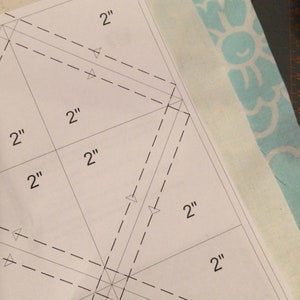 May include: A white paper template with dashed lines and markings for a sewing project. The template is marked with 2" measurements.
