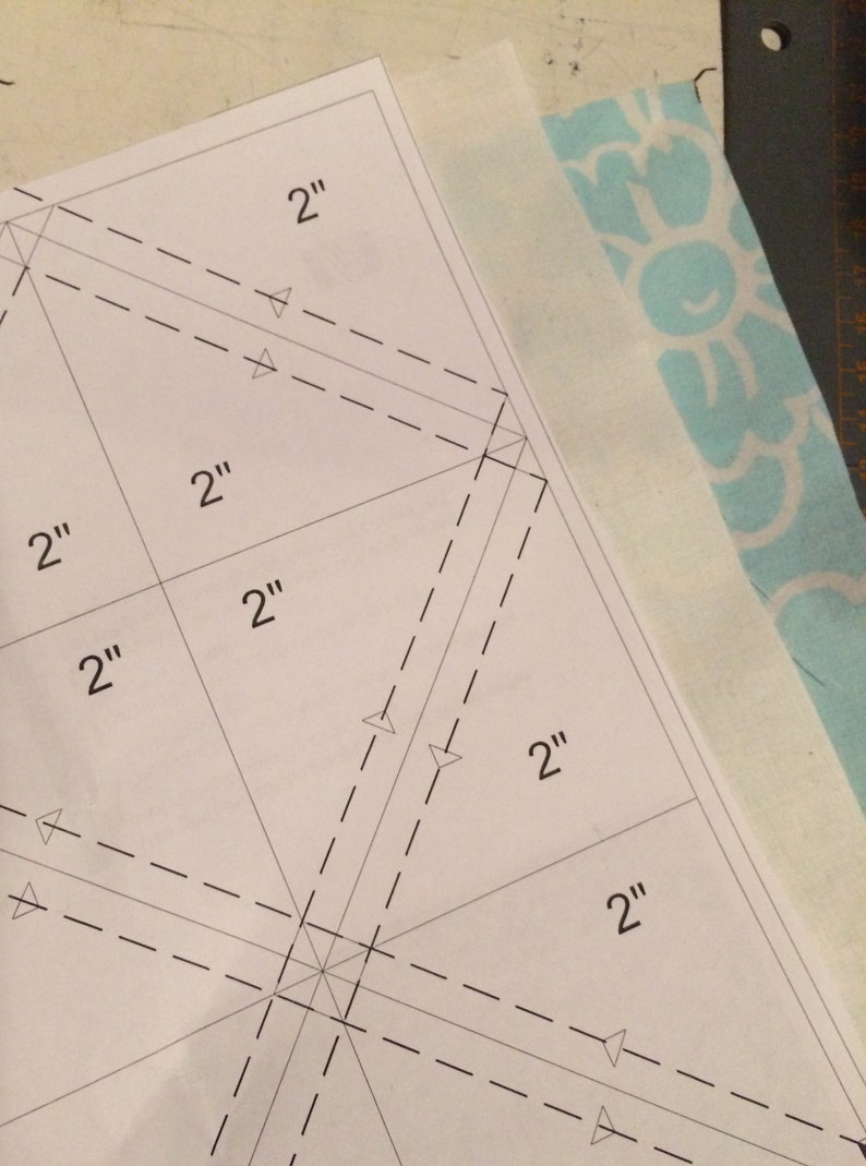 May include: A white paper template with dashed lines and markings for a sewing project. The template is marked with 2" measurements.