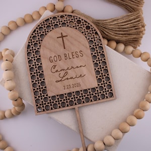 May include: Wooden cake topper with a cross and the text "God Bless Cameron Louie 2.23.2025" in a decorative arch design.
