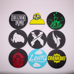 May include: Nine circular designs with various graphics and text. The designs include a white mammoth, a robot, a green eye on a yellow figure, and the text "SULLIVAN KING", "LEVITY", and "CRANKDAT". The backgrounds are black, white, and light blue.