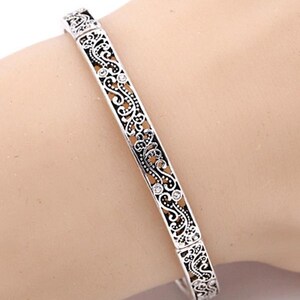 May include: A silver bangle bracelet with an intricate filigree design and small clear stones.