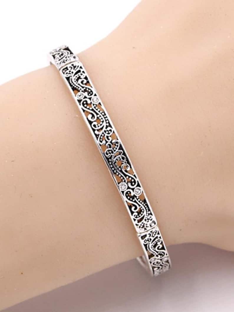May include: A silver bangle bracelet with an intricate filigree design and small clear stones.