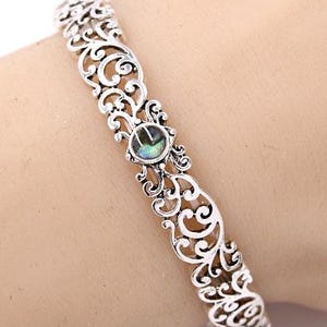 May include: Silver filigree bracelet with an oval, iridescent stone at the centre. The openwork design features scrolling patterns. This cuff bracelet is a piece of jewellery.