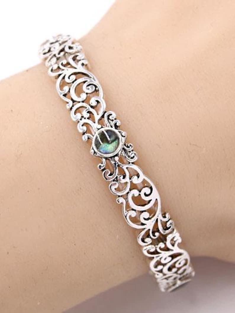 May include: Silver filigree bracelet with an oval, iridescent stone at the centre. The openwork design features scrolling patterns. This cuff bracelet is a piece of jewellery.