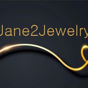 以下が含まれることがあります： 暗い灰色の背景に「Jane2Jewelry」という金色の文字。 下部には、右側でループする、光る効果のある曲線的な金色の線があります。 シンプルでエレガントなデザインです。
