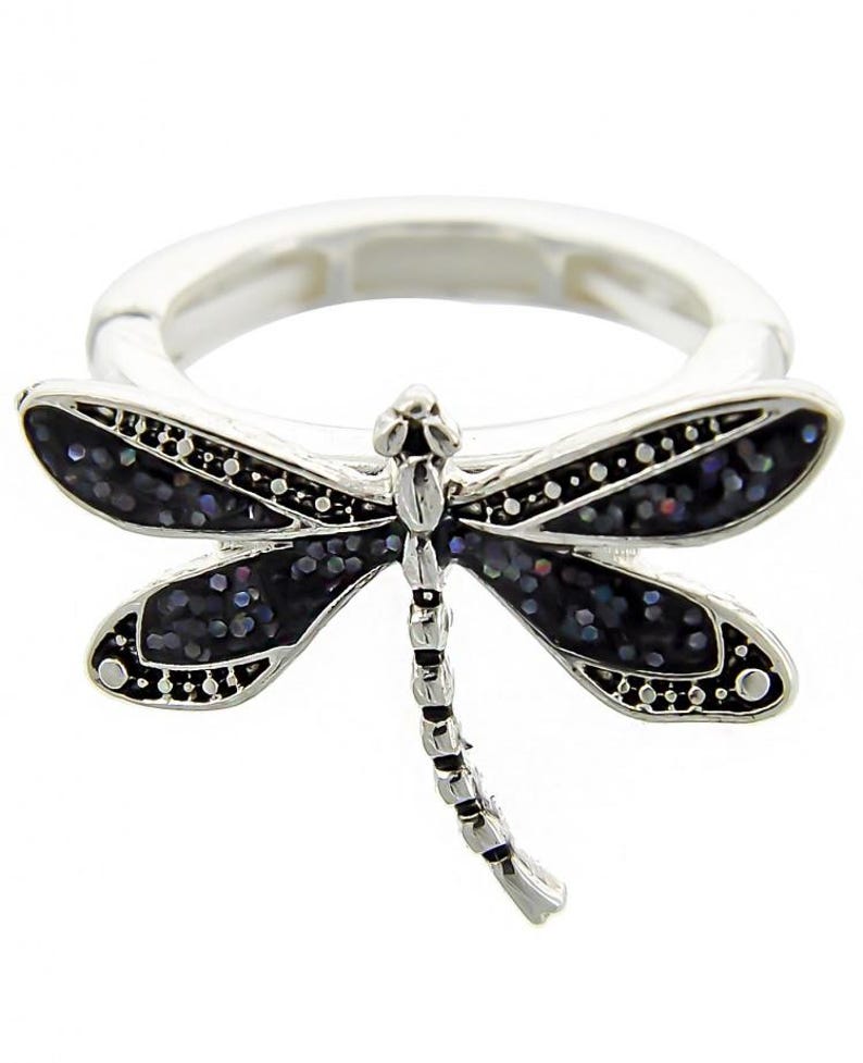 May include: A silver ring with a black dragonfly design. The dragonfly has iridescent wings and a detailed body.