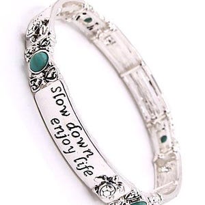 Peut inclure: Bracelet extensible argent&eacute; avec des accents turquoise et l'inscription "slow down enjoy life". Le bracelet pr&eacute;sente des motifs d&eacute;coratifs de tortues et de fleurs. Un accessoire &eacute;l&eacute;gant.