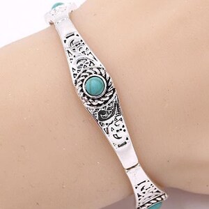 May include: Silver bracelet with an ornate design and turquoise stones.