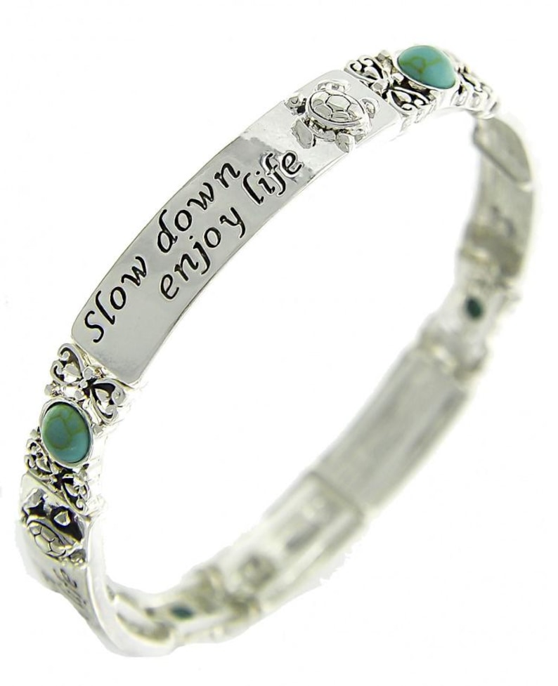 Peut inclure: Bracelet argent&eacute; avec l'inscription "slow down enjoy life". Le bracelet pr&eacute;sente des pierres de couleur turquoise et des motifs de tortues. Le bracelet est de style extensible.