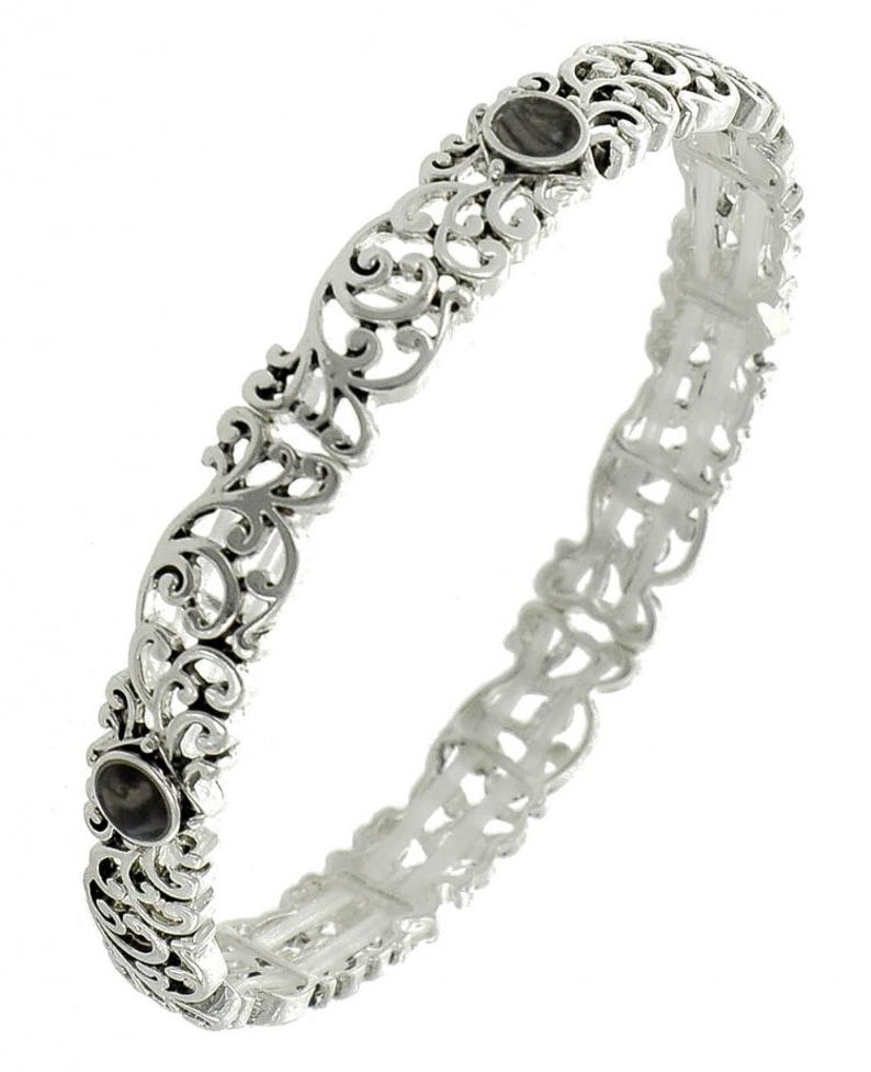 May include: A silver bangle bracelet with an openwork design. The bracelet features intricate scrollwork and two oval, dark grey stones. The metal has a polished finish, and the design is symmetrical.